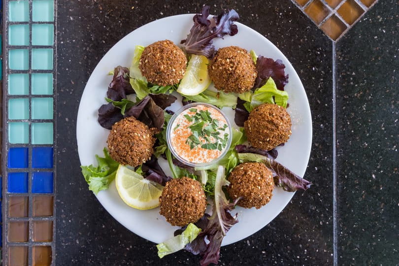 A white plate of falafel, lettuce, lemon wedges, and a dipping sauce with parsley and paprika.