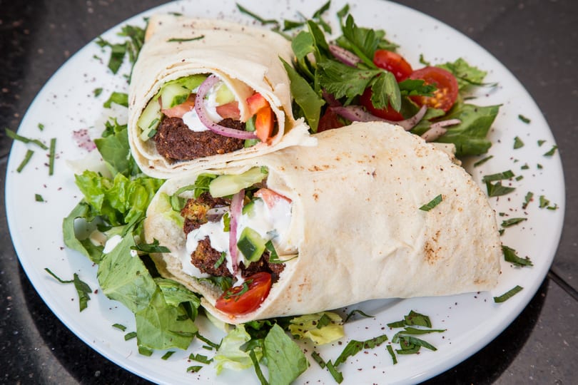 Two falafel wraps with fresh vegetables and sauce, served on a white plate with a side salad.