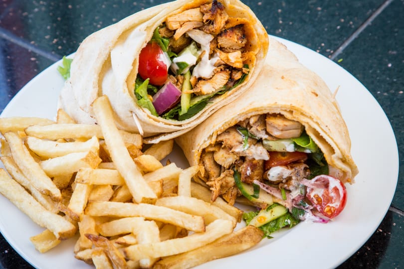Two chicken shawarma wraps with fresh vegetables and white sauce, served with golden french fries.