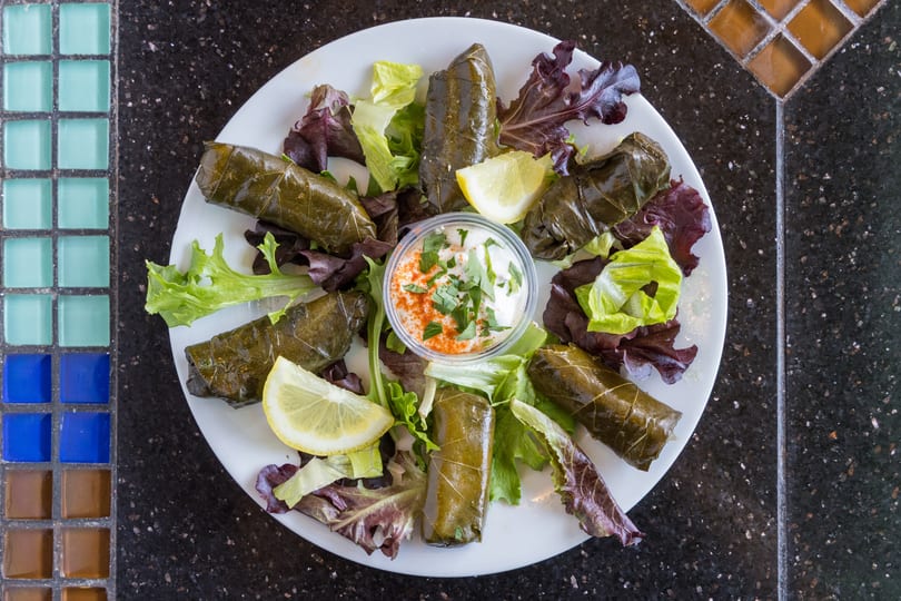 Plate of dolmades (stuffed grape leaves) with lettuce, lemon wedges, and a side of dipping sauce.