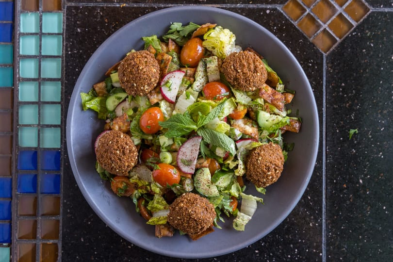 Overhead view of a vibrant falafel salad with cherry tomatoes, radishes, cucumbers, and mint.